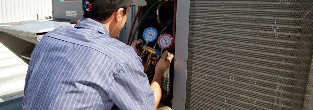 HVAC technician servicing a condenser unit in Ponca City
